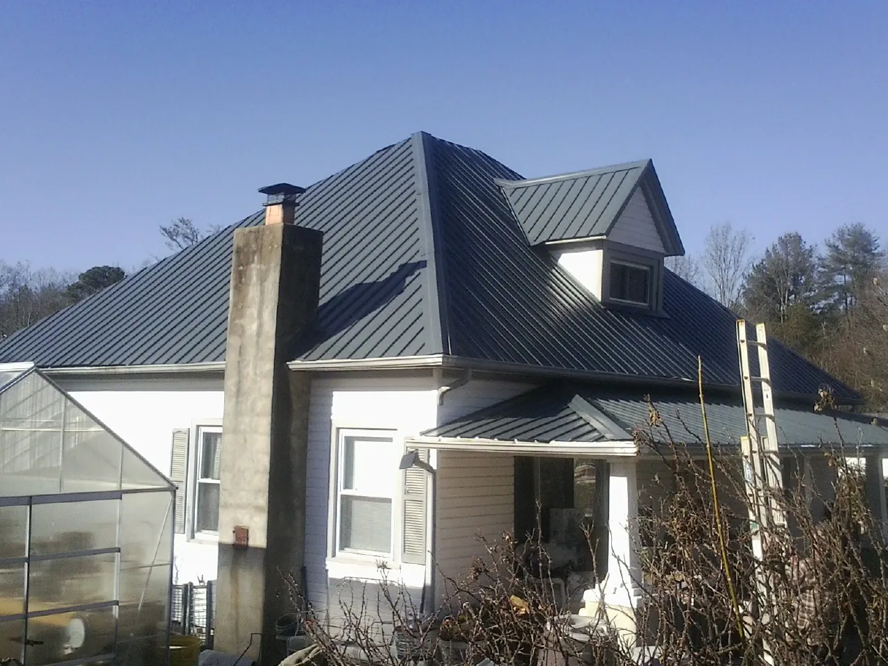 Dark blue standing seam metal roof on a white farmhouse with dormer — Slate & Tile Roof Repair by Roofing Brothers in Youngtown