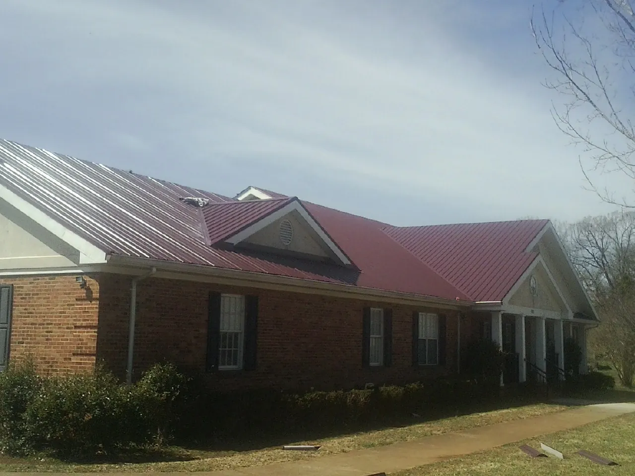 Red metal roof with gabled entries on a long brick building, from a Hail Damage Roof Repair job in Youngtown