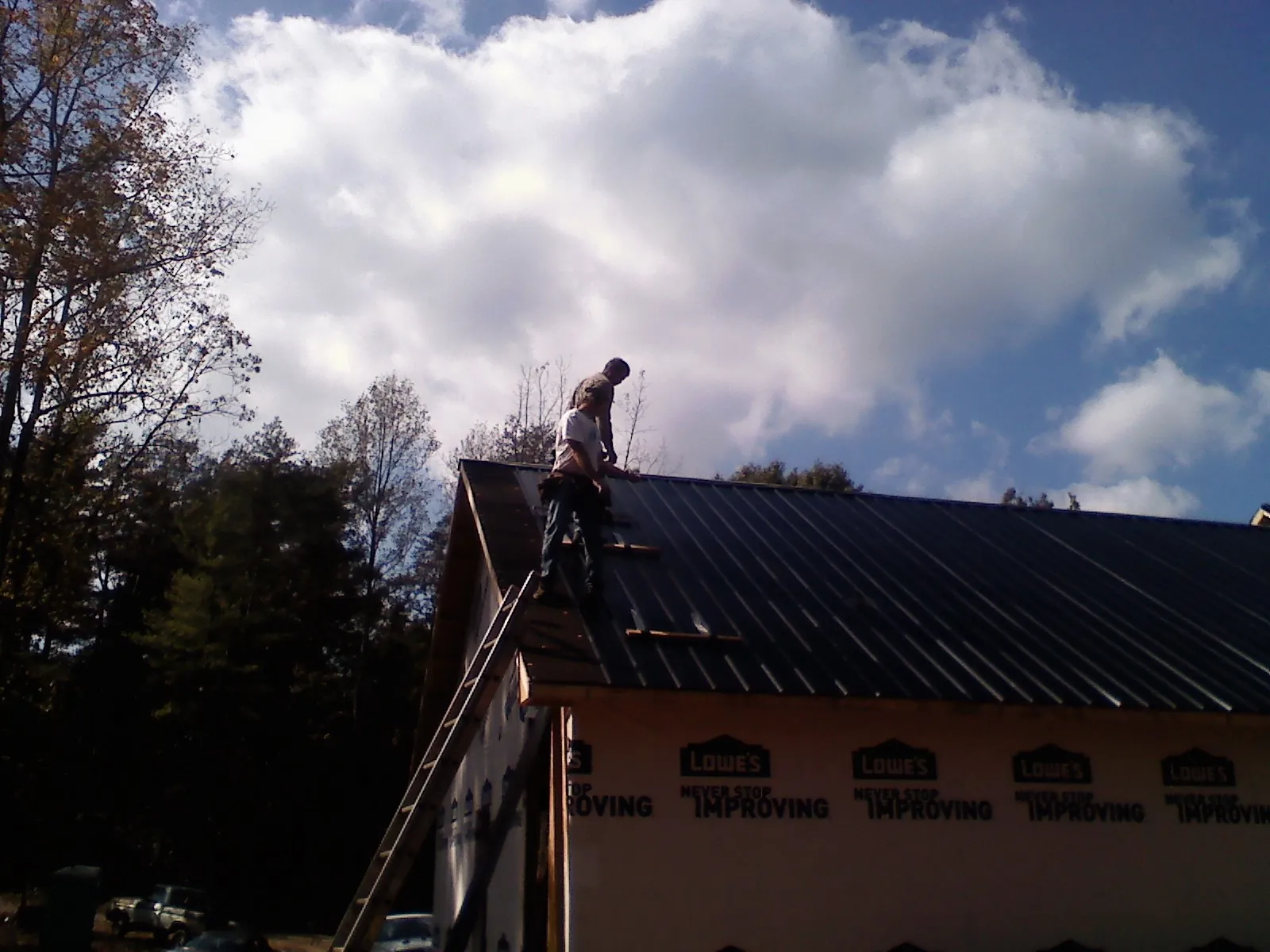 Roofer fastening dark metal panels high against a cloudy sky, from a Roof Inspection job in Youngtown