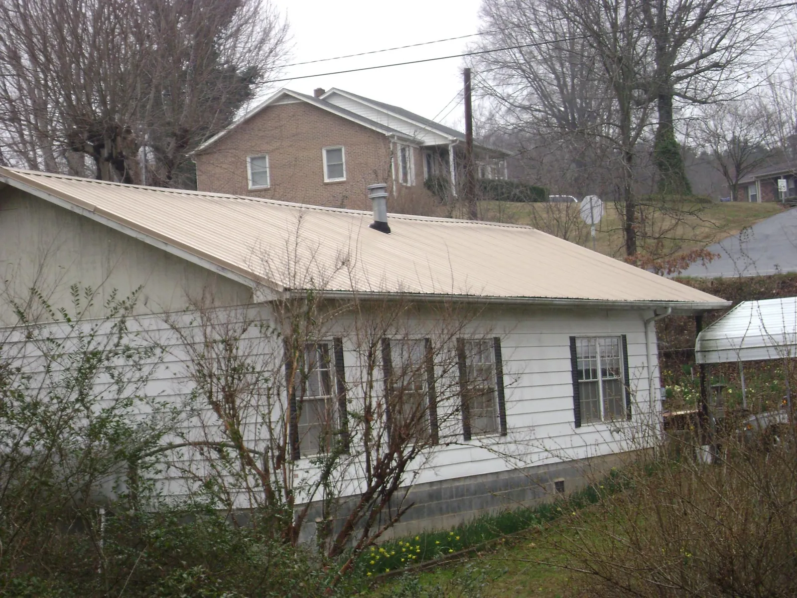 Tan metal roof on a white sided house set into a hillside — Commercial Roofing by Roofing Brothers in Youngtown